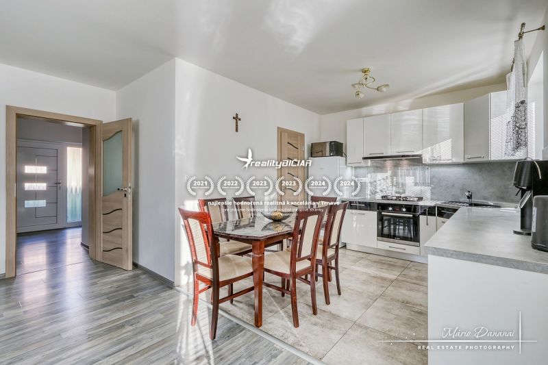 Eine Küche in einem Einfamilienhaus mit Keramikfliesen, einem Holztisch und weißen Schränken.