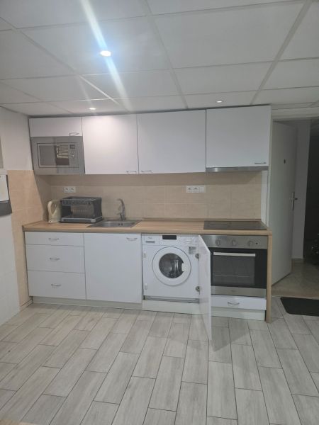 Küche in einer Einzimmerwohnung mit weißer Küchenzeile und Boden in Holzoptik.