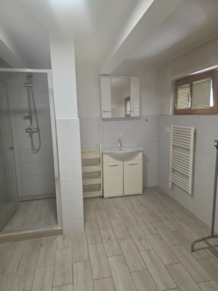 Badezimmer mit Duschkabine, Waschbecken und Boden mit Holzdekor in einer Einzimmerwohnung.