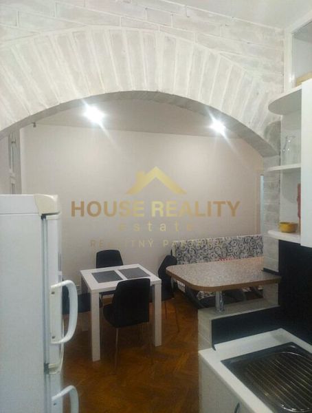 Küche in einer 2-Zimmer-Wohnung mit Backsteinbogen, Tisch und Stühlen, Boden mit Holzdekor.