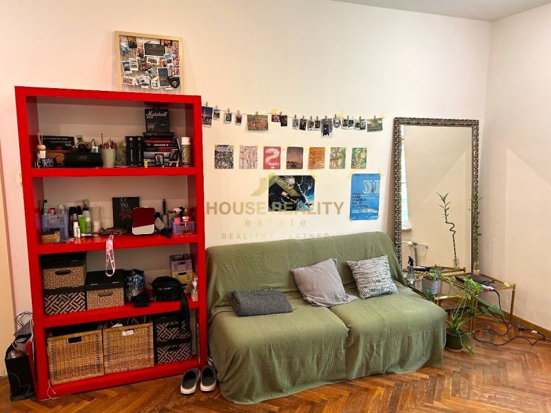Wohnzimmer in einer 2-Zimmer-Wohnung mit rotem Regal und Holzboden.