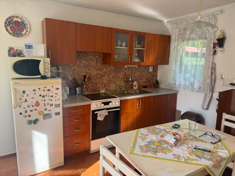 Das Innere der Hütte mit einer älteren Küchenzeile, einem Kühlschrank und einem dekorativen Teller an der Wand.