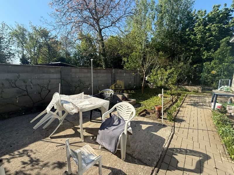 Der Garten des Ferienhauses in Sekule mit Plastikmöbeln und Bäumen am Rand.