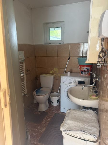 Badezimmer in der Hütte mit Toilette, Waschmaschine und Waschbecken. Fliesen an den Wänden.