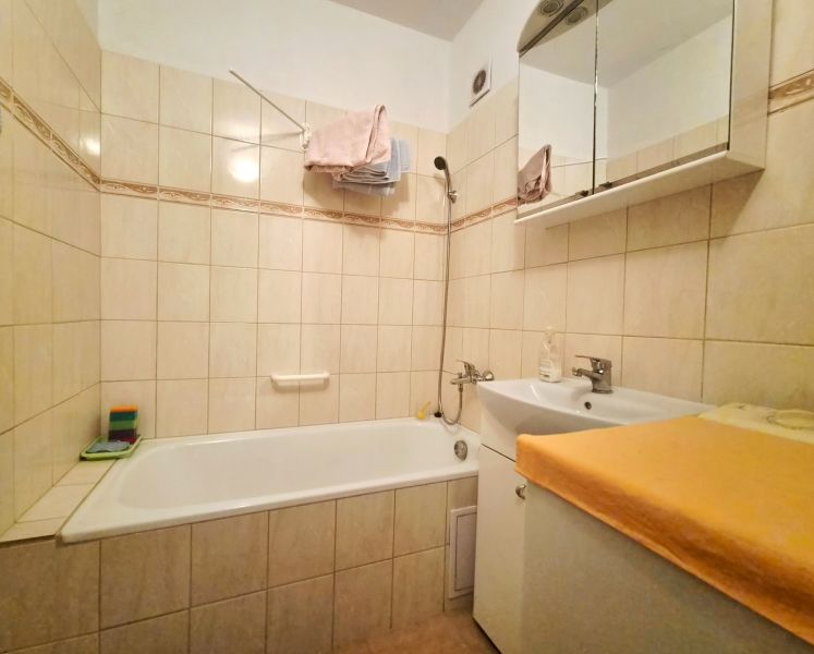 Badezimmer mit Dusche und Waschbecken in einer 2-Zimmer-Wohnung, gefliest mit hellen Fliesen.