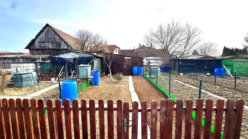 Der Garten in Hlboké mit ländlichen Gebäuden und Fässern zwischen den Zäunen.