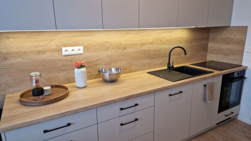 Küche in einer 3-Zimmer-Wohnung mit Holzboden, heller Küchenzeile und schwarzem Spülbecken.