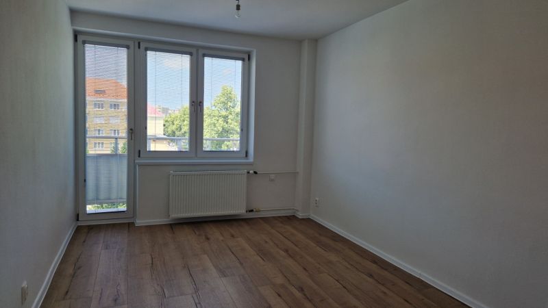 Ein Zimmer in einer 3-Zimmer-Wohnung mit einem Holzboden, einem großen Fenster und einem Heizkörper.