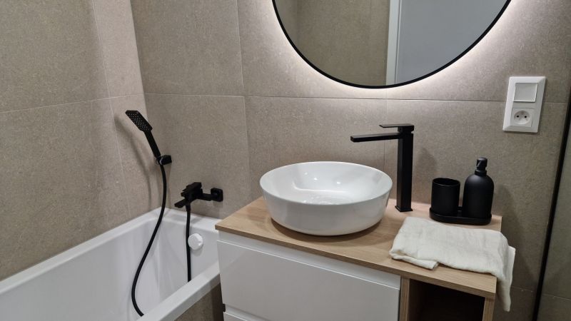 Badezimmer in einer 3-Zimmer-Wohnung mit rundem Spiegel und modernen Armaturen.