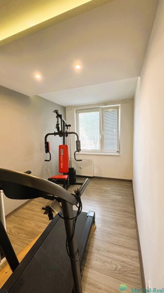 Innenraum einer 4-Zimmer-Wohnung mit Laufband und Kraftstation, Boden mit Holzdekor.