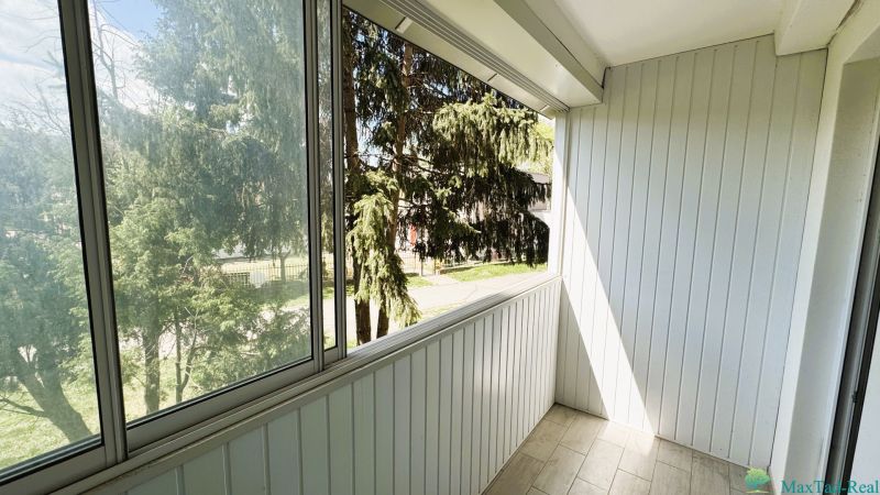 Ein verglaster Balkon in einer 4-Zimmer-Wohnung mit Blick auf Bäume, weiße Holzwand.