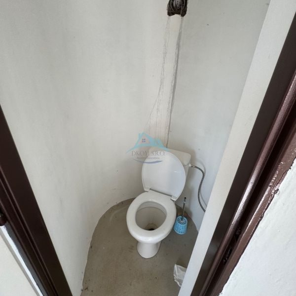 Einfache Toilette in einer Hütte mit unverkleideter Wand und Plastik-WC.