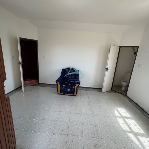 Ein Zimmer mit einem Sessel, weißen Wänden, Fliesenboden und einer Tür, die zu einer Toilette in der Hütte führt.