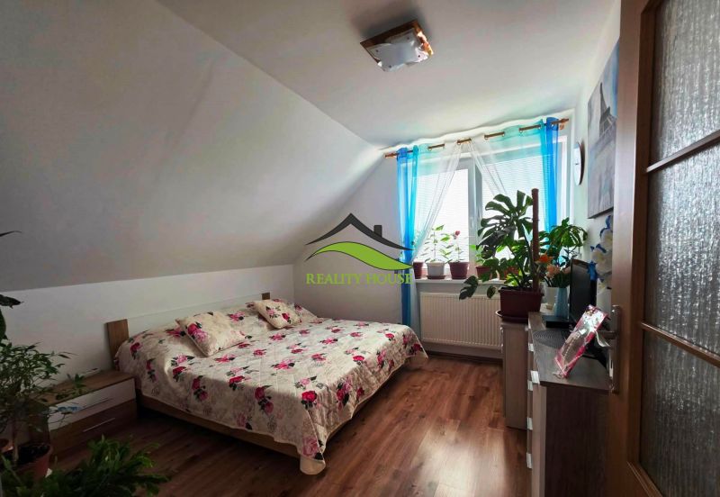 Ein Schlafzimmer in einem Einfamilienhaus mit einem Bett, einem Boden in Holzoptik und Zimmerpflanzen.