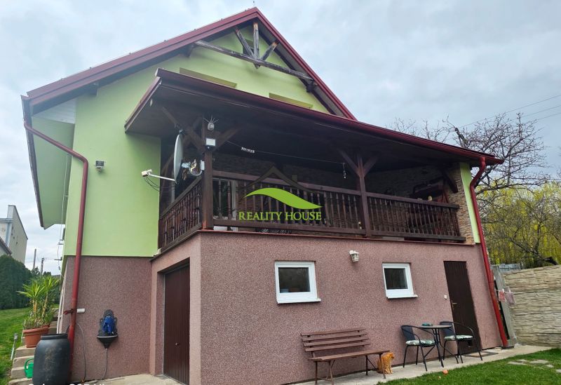 Ein Einfamilienhaus in Klokočov mit überdachter Terrasse, Grünflächen und Gartenmöbeln.