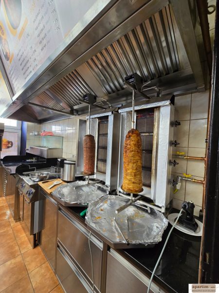 Eine Küche in einem Gastronomiebereich mit Ausstattung zur Zubereitung von Kebab, einschließlich Dunstabzugshaube.