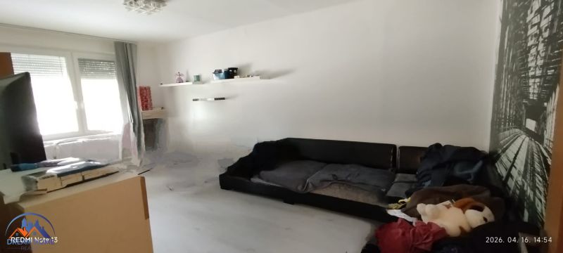 Wohnzimmer in einer 2-Zimmer-Wohnung mit weißen Wänden und einem schwarzen Sofa.