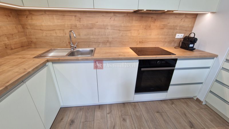 Küche mit Arbeitsplatte in Holzdekor und eingebauten Geräten in einer 2-Zimmer-Wohnung.