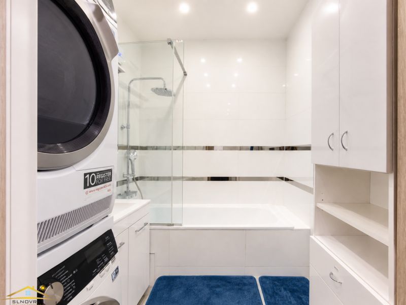 Badezimmer in einer 3-Zimmer-Wohnung mit Badewanne, Waschmaschine und weißen Möbeln.