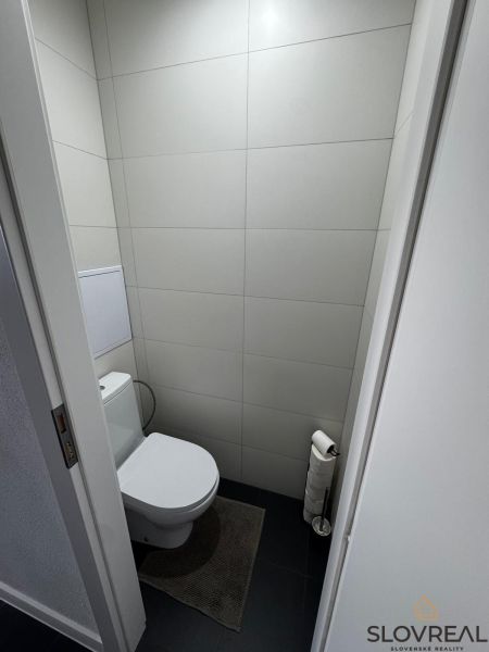 Toilette in einer 3-Zimmer-Wohnung mit minimalistischen grauen Fliesen und dunklem Boden.