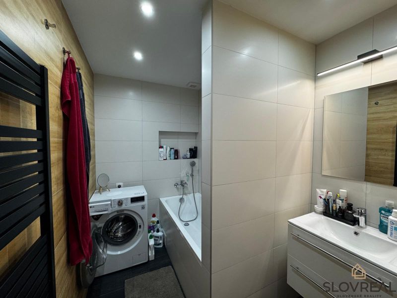 Badezimmer in einer 3-Zimmer-Wohnung mit Badewanne, Waschmaschine und Holzwanddekor.