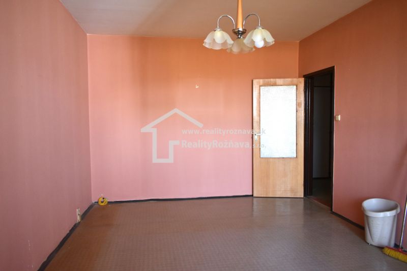 Ein Zimmer mit rosa Wänden und braunem Boden in einer 3-Zimmer-Wohnung.