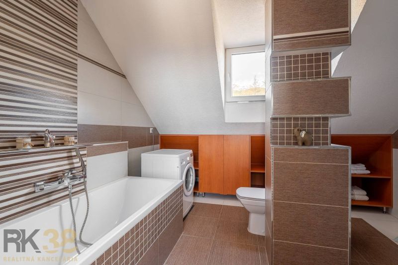 Badezimmer mit Satteldach, Badewanne, Waschmaschine und braunen Fliesen in einer 4-Zimmer-Wohnung.