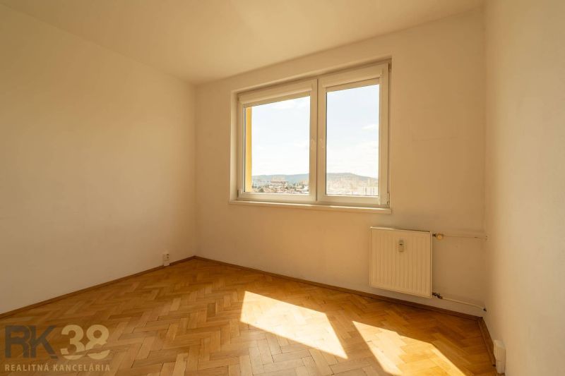 Ein Zimmer mit Fenster, Heizkörper und einem Boden mit Holzdekor in einer 4-Zimmer-Wohnung.