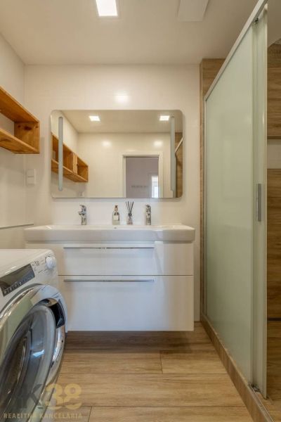 Badezimmer in einer 4-Zimmer-Wohnung, Waschbecken mit Spiegel, Waschmaschine, Boden mit Holzdekor.