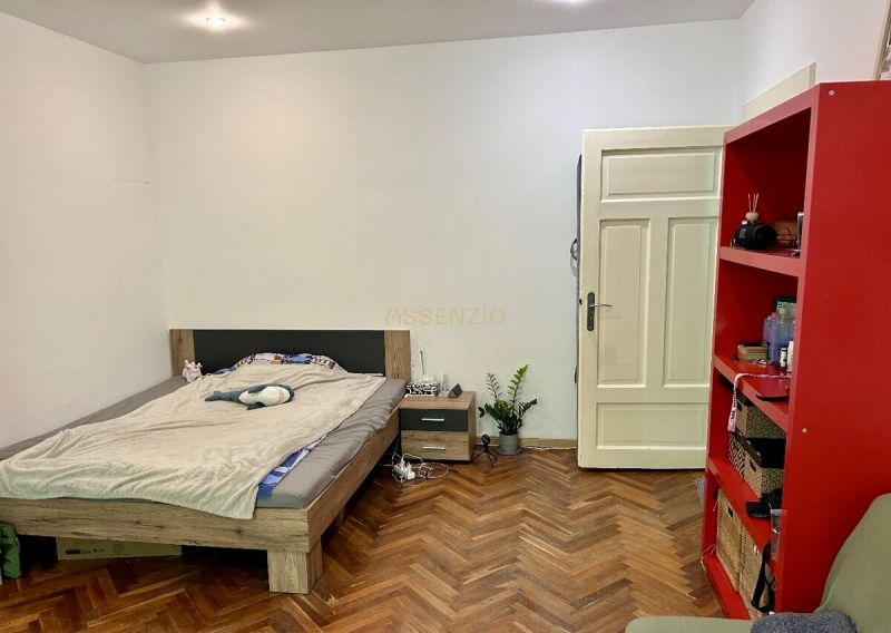 Schlafzimmer in einer 2-Zimmer-Wohnung mit Bett, rotem Regal und Boden in Holzoptik.