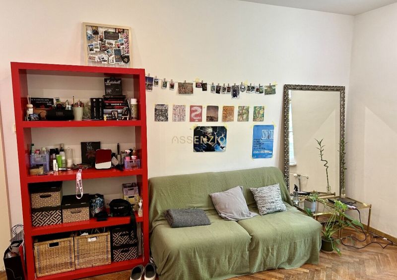 Wohnzimmer in einer Zweizimmerwohnung mit einem grünen Sofa, einem roten Regal und einem Boden mit Holzdekor.