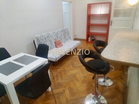 Wohnzimmer einer Zweizimmerwohnung mit Holzboden, Esstisch und Barhockern.