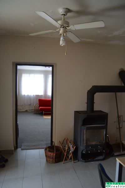 In einem Einfamilienhaus gibt es einen Deckenventilator, einen Kaminofen und ein rotes Sofa im Hintergrund.