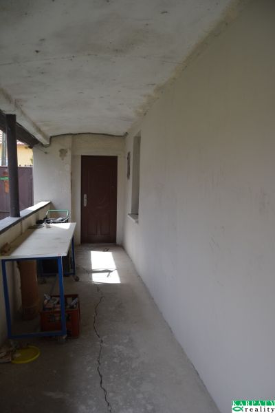 Ein Flur mit weißen Wänden, Risse im Boden, ein Tisch, Türen in einem Einfamilienhaus.