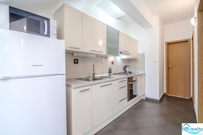 Helle Küche im Ferienapartment mit Einbaugeräten und Fliesenboden.