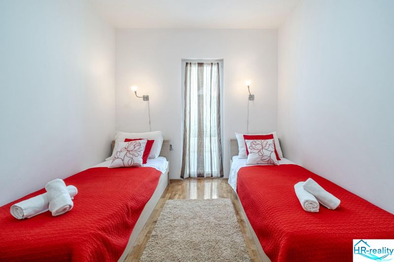 Ferienwohnung mit zwei Betten, roter Decke und Holzboden.