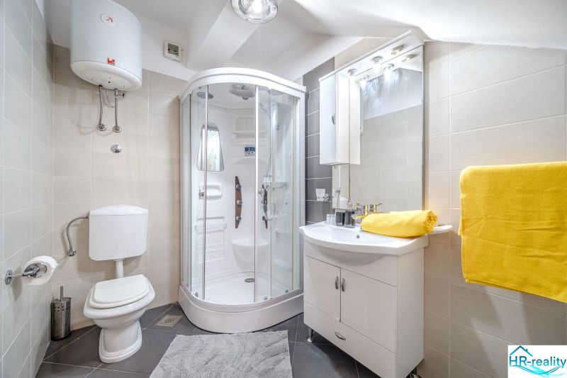 Badezimmer in einer Ferienwohnung mit moderner Duschkabine und leuchtend gelben Handtüchern.
