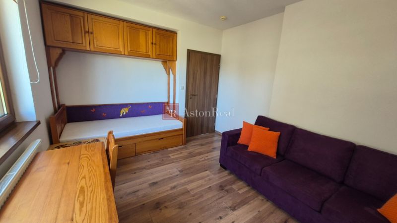 Ferienwohnung mit Sofa, Bett, Schrank und Boden in Holzoptik.