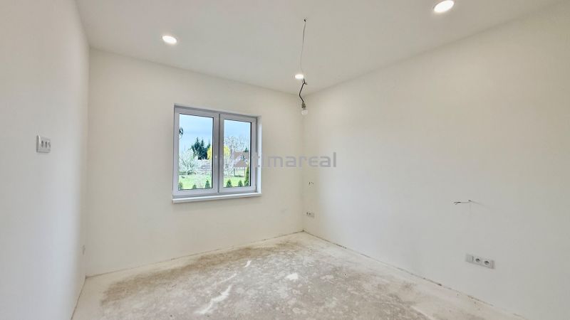 Ein leerer Raum in einem Einfamilienhaus mit weißen Wänden und einem Fenster mit Blick nach draußen.