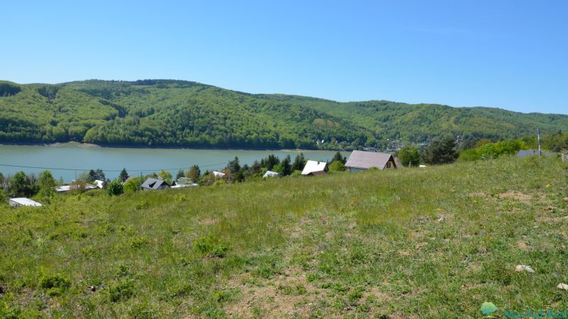 Freizeitgrundstücke in Nová Kelča mit Blick auf grüne Hügel und Wasserfläche.