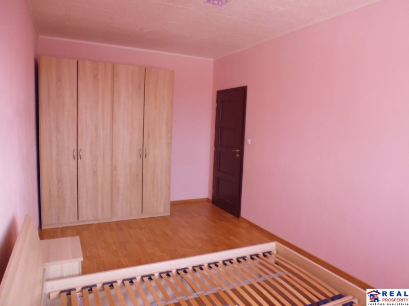 Ein Zimmer in einer 2-Zimmer-Wohnung mit rosa Wänden, einem Schrank und einem Boden in Holzoptik.