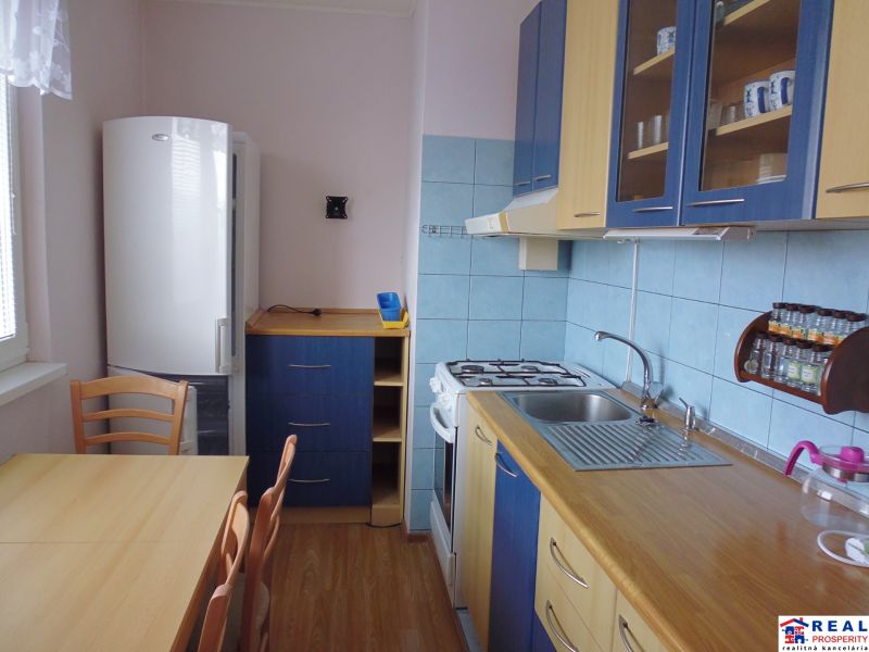 Küchenbereich in einer 2-Zimmer-Wohnung mit Stühlen, Holzboden, blaue Fliesen.