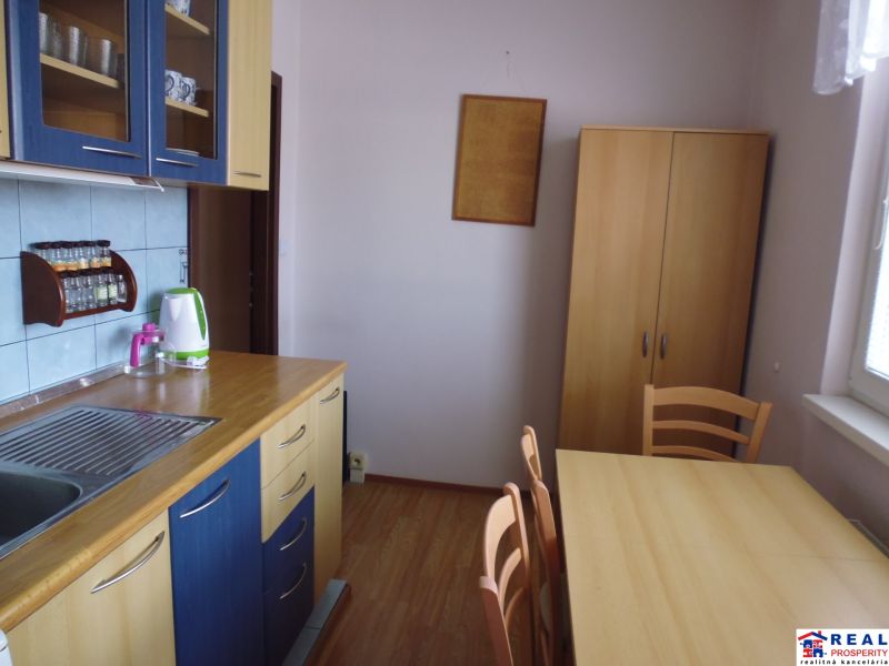 Küche in einer 2-Zimmer-Wohnung mit Holzboden, Esstisch und Regalen.