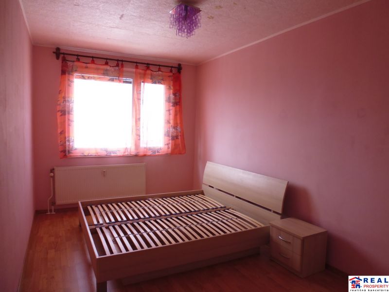 Schlafzimmer mit hellrosa Wänden, einem Bett und einem Boden mit Holzdekor in einer Zweizimmerwohnung.