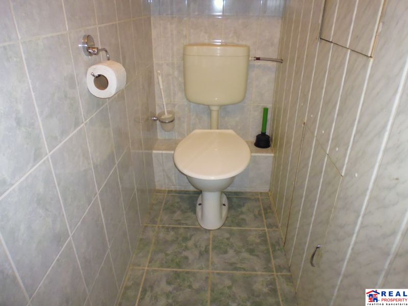 Badezimmer mit Toilette in einer 2-Zimmer-Wohnung mit gefliesten Wänden und Boden.