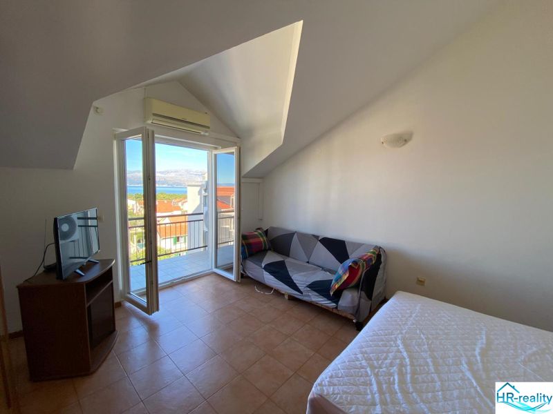 Zimmer in einer Ferienwohnung mit Balkon und Meerblick, Fernseher und Sofa.