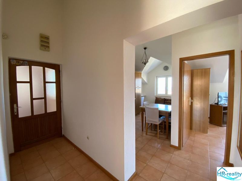 Flur in einer Ferienwohnung mit Keramikboden, Essbereich und Zimmer im Hintergrund.