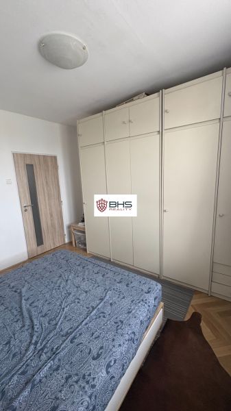 Ein Schlafzimmer mit einem Bett, einem Schrank und einem Boden mit Holzdekor in einer 2-Zimmer-Wohnung.