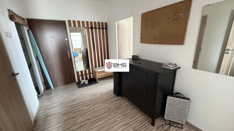 Der Flur in einer 2-Zimmer-Wohnung mit einem Boden in Holzoptik, einem Spiegel und einer schwarzen Kommode.