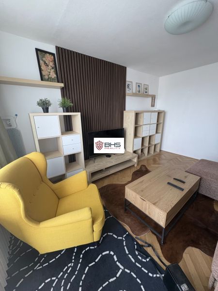 Wohnzimmer mit Holzboden, gelbem Sessel und Couchtisch aus Holz.